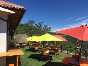 Un espacio al aire libre con mesas y sillas, sombrillas y vistas a un paisaje montañoso.