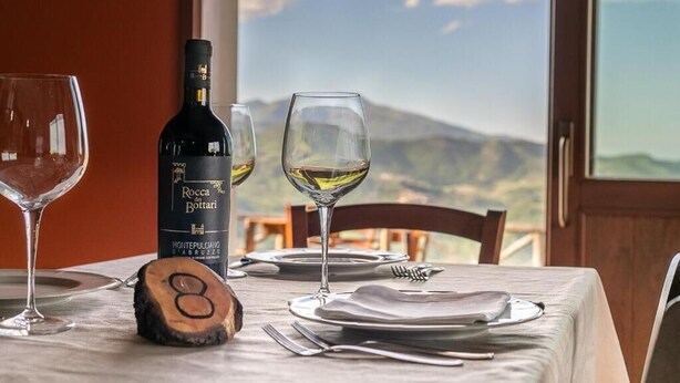A table set with wine glasses and a bottle of Rocca Bottari wine, with a scenic mountain view in the background. - Agriturismo Lo Scoiattolo (Montorio al Vomano)