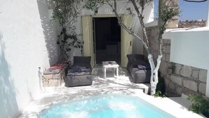 Un espacio pequeño de piscina al aire libre con un banco de piedra, dos sofás y una mesa.