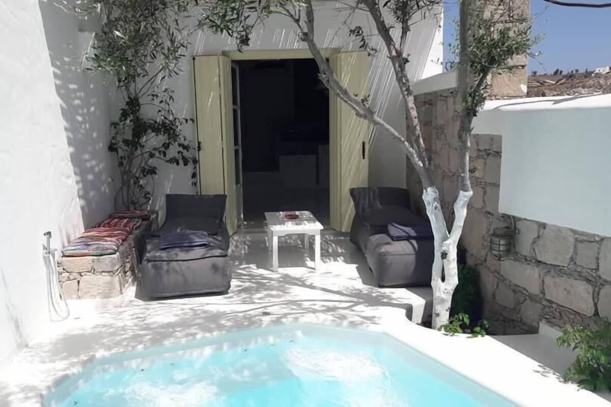 A small outdoor pool area with a stone bench, two sofas, and a table.
