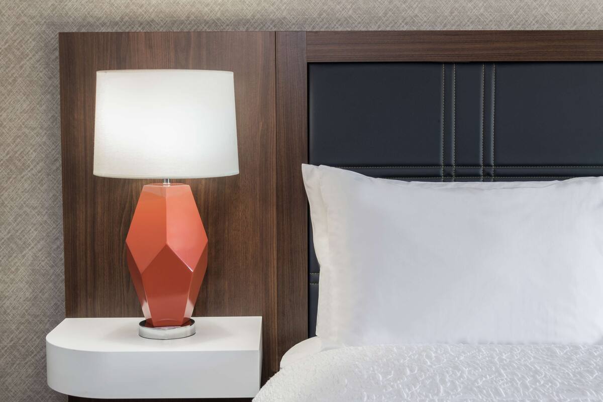 A bed with a white pillow and a nightstand with a red lamp.