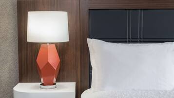 A bed with a white pillow and a nightstand with a red lamp.