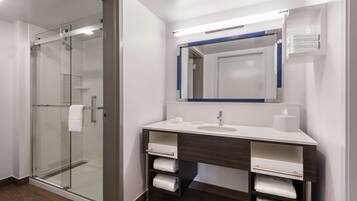 Un baño moderno con cabina de ducha de vidrio, un lavamanos blanco con espejo y toalleros integrados.