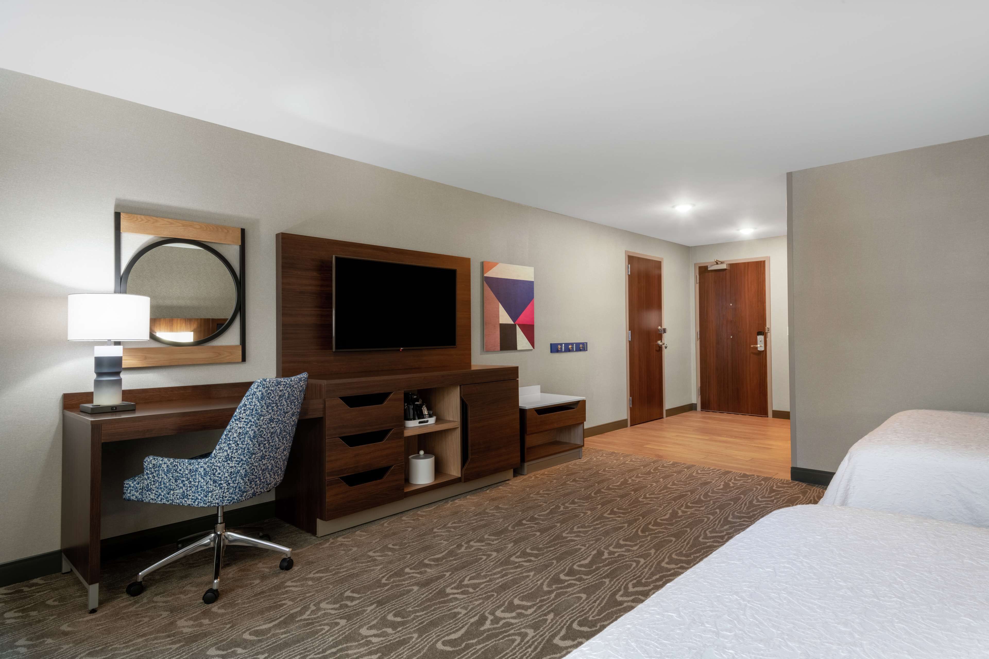 Ein Hotelzimmer mit Bett, Schreibtisch mit Stuhl, Fernseher, Spiegel und einer Tür.