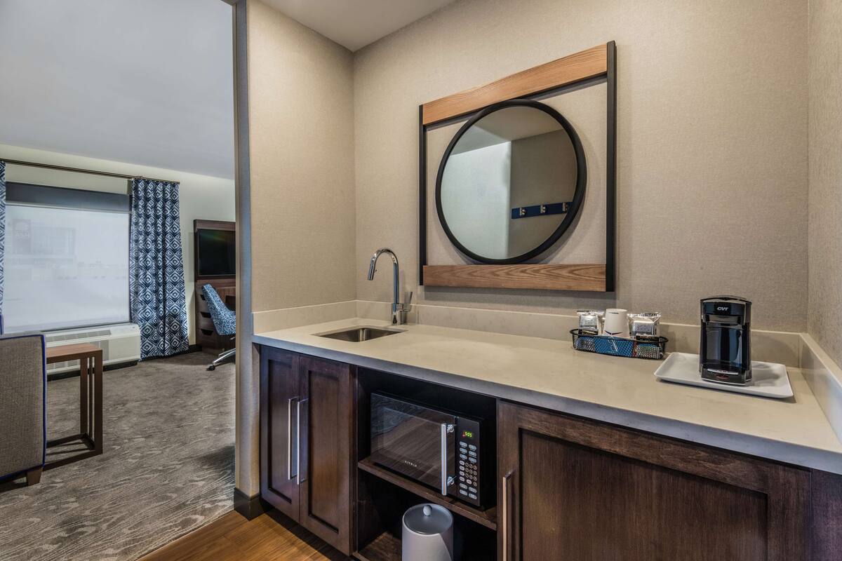 A modern bathroom with a sink, mirror, and coffee maker.