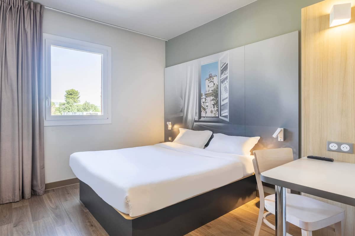 Une chambre d’hôtel avec un lit, un bureau et une fenêtre avec des rideaux.