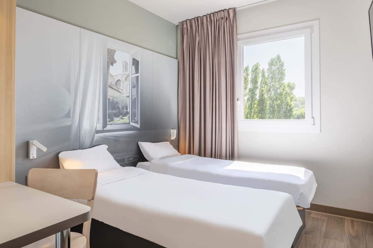 Une chambre d’hôtel avec deux lits, un bureau et une fenêtre avec des rideaux.