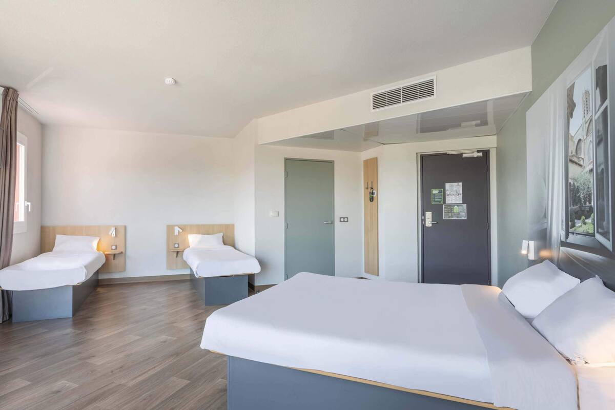 Une chambre d’hôtel avec deux lits simples et un lit double, un plancher en bois et une grande fenêtre donnant sur un beau paysage.