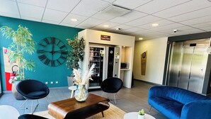 Un hall d’entrée moderne avec un mur de couleur turquoise, une grande horloge, un comptoir d’accueil et un canapé bleu.