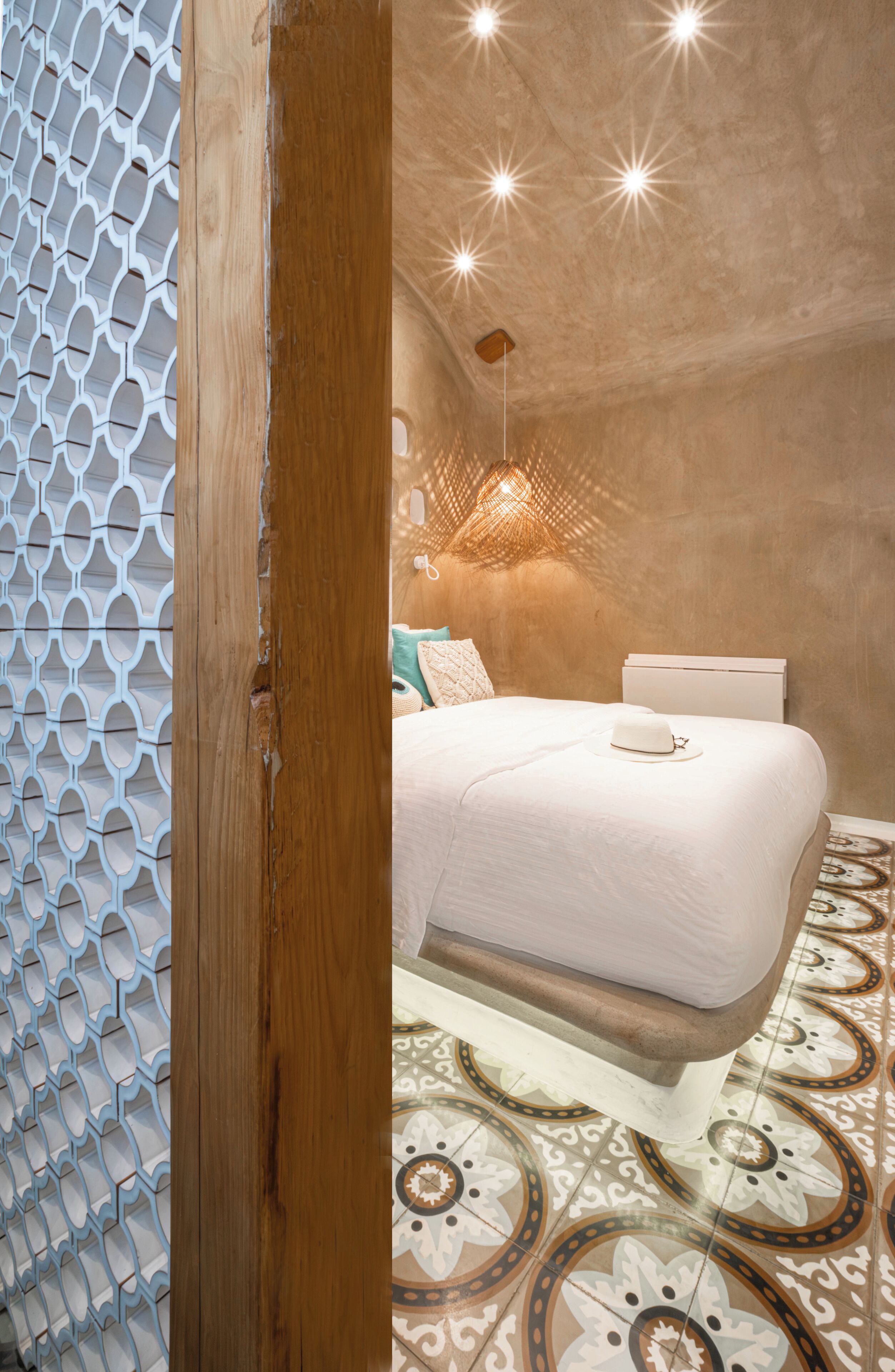 A bedroom with a patterned floor, a bed with a white headboard, and a wall with a geometric design.