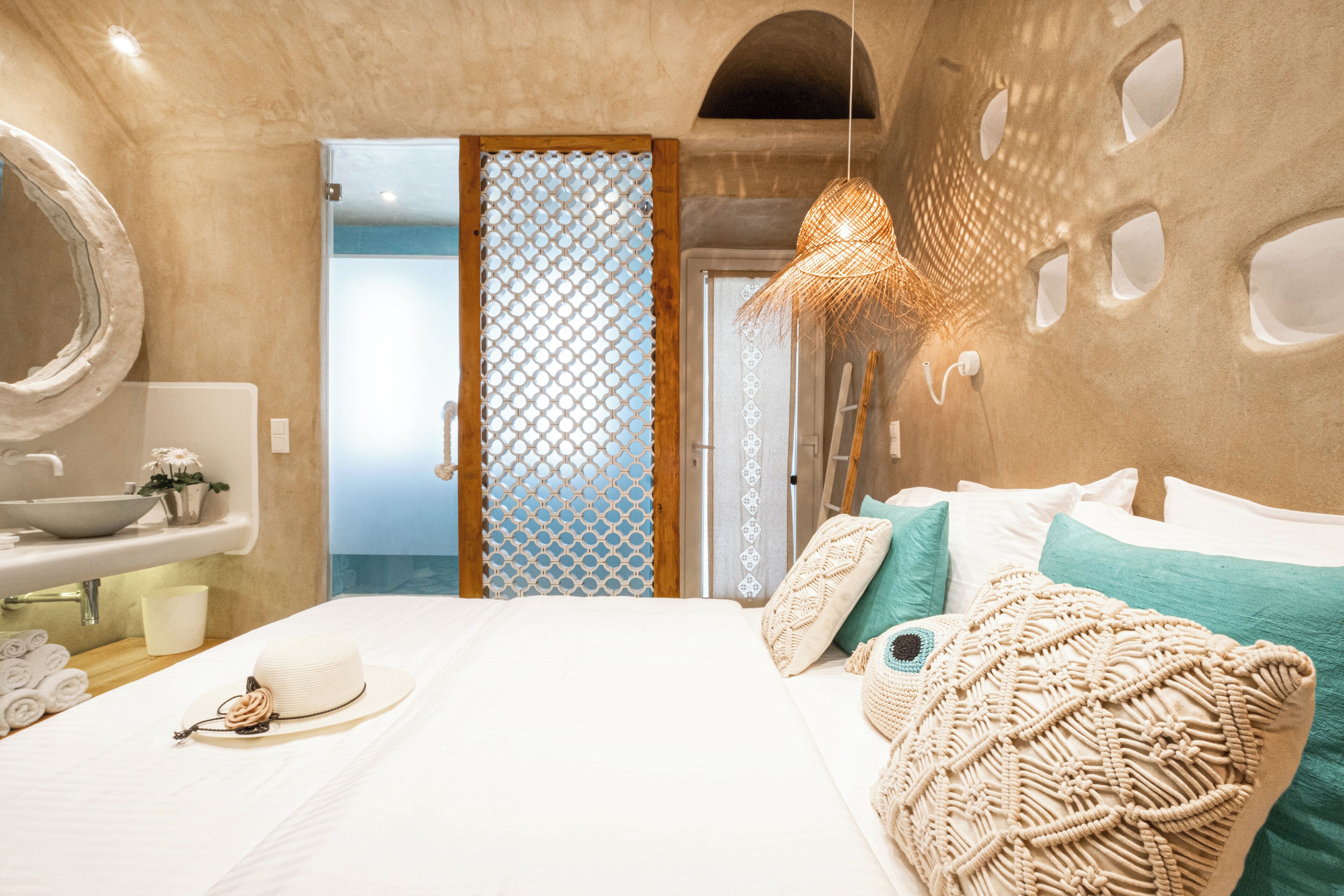 A modern hotel room with a large bed, a bathroom with a sink and mirror, and a decorative wall.