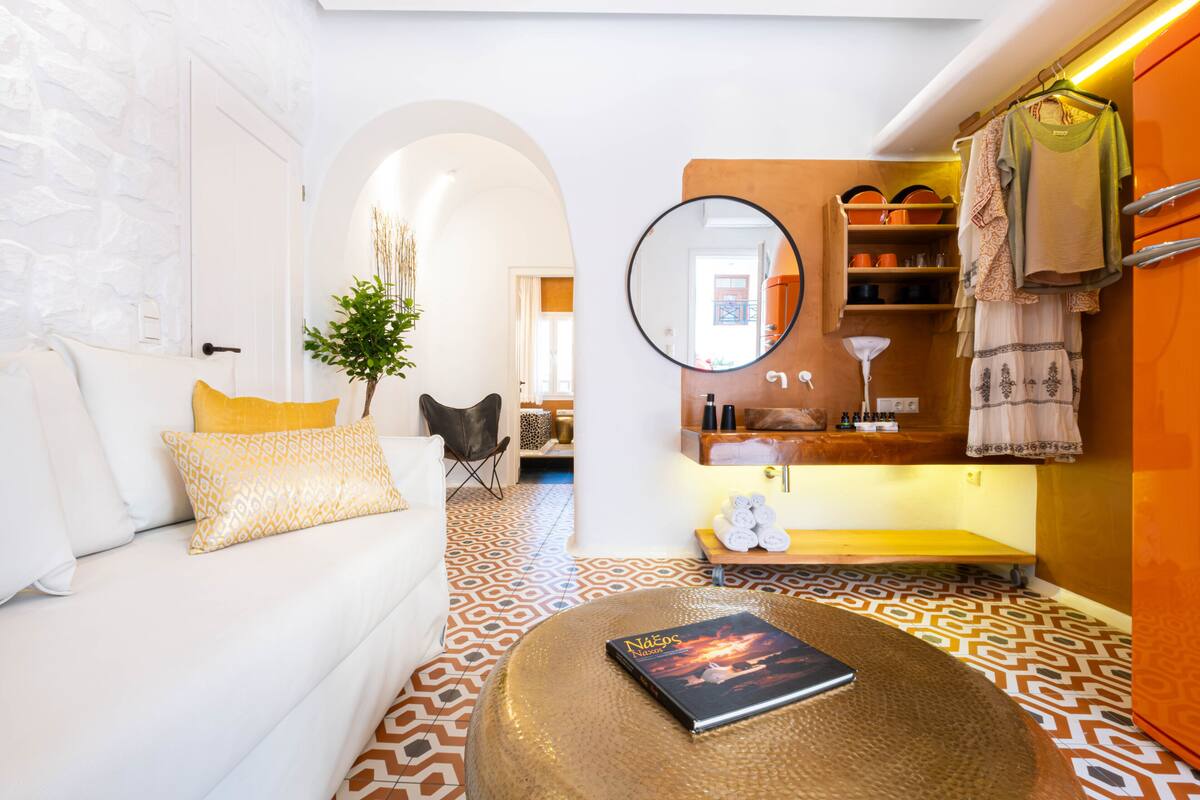 Ein modernes Wohnzimmer mit einem weißen Sofa, gemusterten Kissen, einem runden Couchtisch mit einem Buch, einem Spiegel und einem gestalteten Boden.