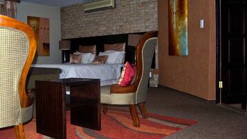 A hotel room with a brick wall, a bed with pillows, a chair, a small table, and a carpet.