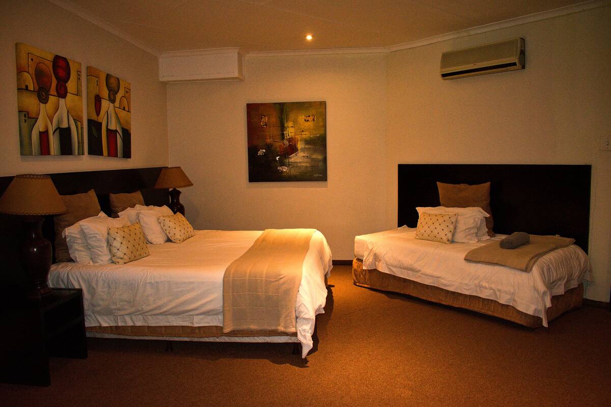 A hotel room with two beds, a painting on the wall, and an air conditioning unit.