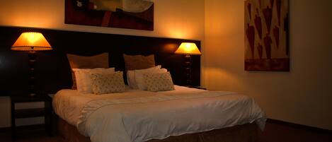 A hotel room with a large bed, two bedside lamps, a headboard, and two wall-mounted paintings.