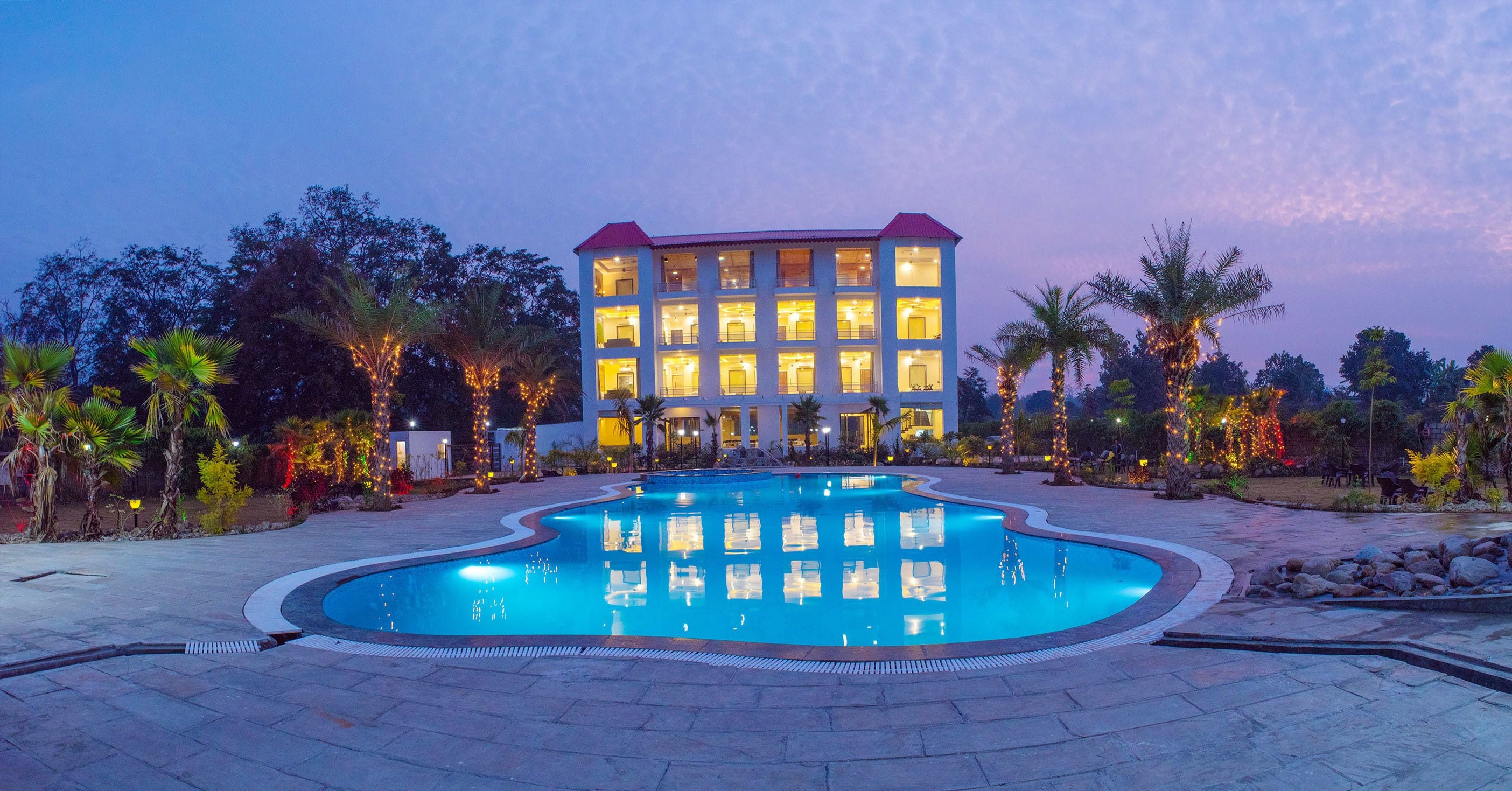 A hotel with a swimming pool, palm trees, and string lights.