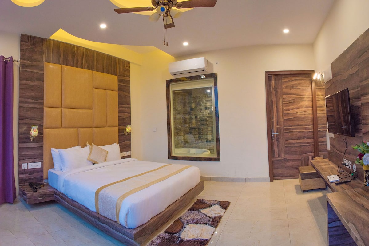 Un dormitorio moderno con una cama grande, ventilador de techo, unidad de aire acondicionado, televisor y una pared de acento de madera.