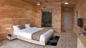 A wooden-paneled bedroom with a bed, bedside table, and a TV mounted on the wall. - The Darien Resort (Kaladhungi)