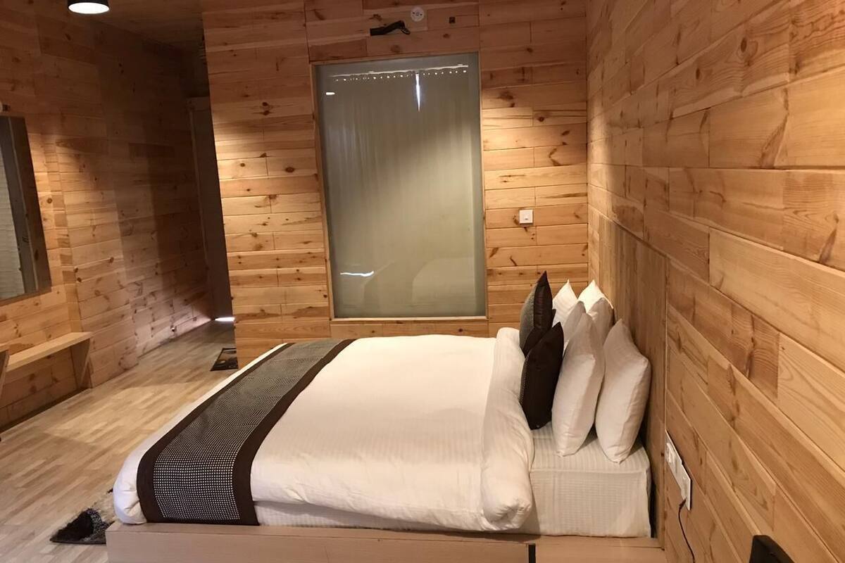 Habitación con paneles de madera, una cama, una mesita y televisor instalado en la pared.