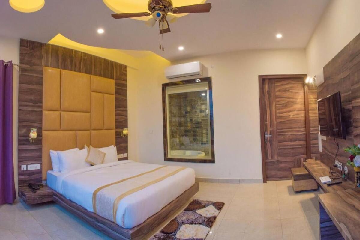 Una habitación de hotel moderna con una cama grande, un ventilador de techo, un equipo de aire acondicionado, un televisor y una pared decorativa de madera.