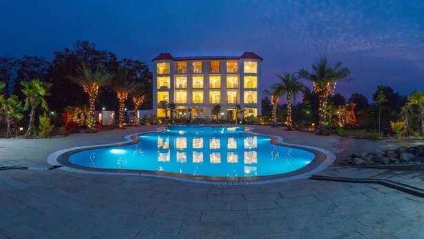 A hotel with a swimming pool, surrounded by palm trees and illuminated by string lights. - The Darien Resort (Kaladhungi)