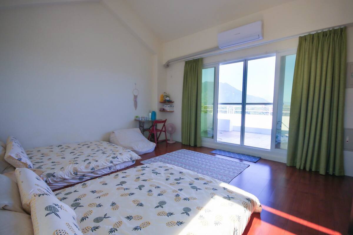 Habitación de hotel con dos camas, una mesita, una silla, un ventanal con cortinas y vistas al exterior.