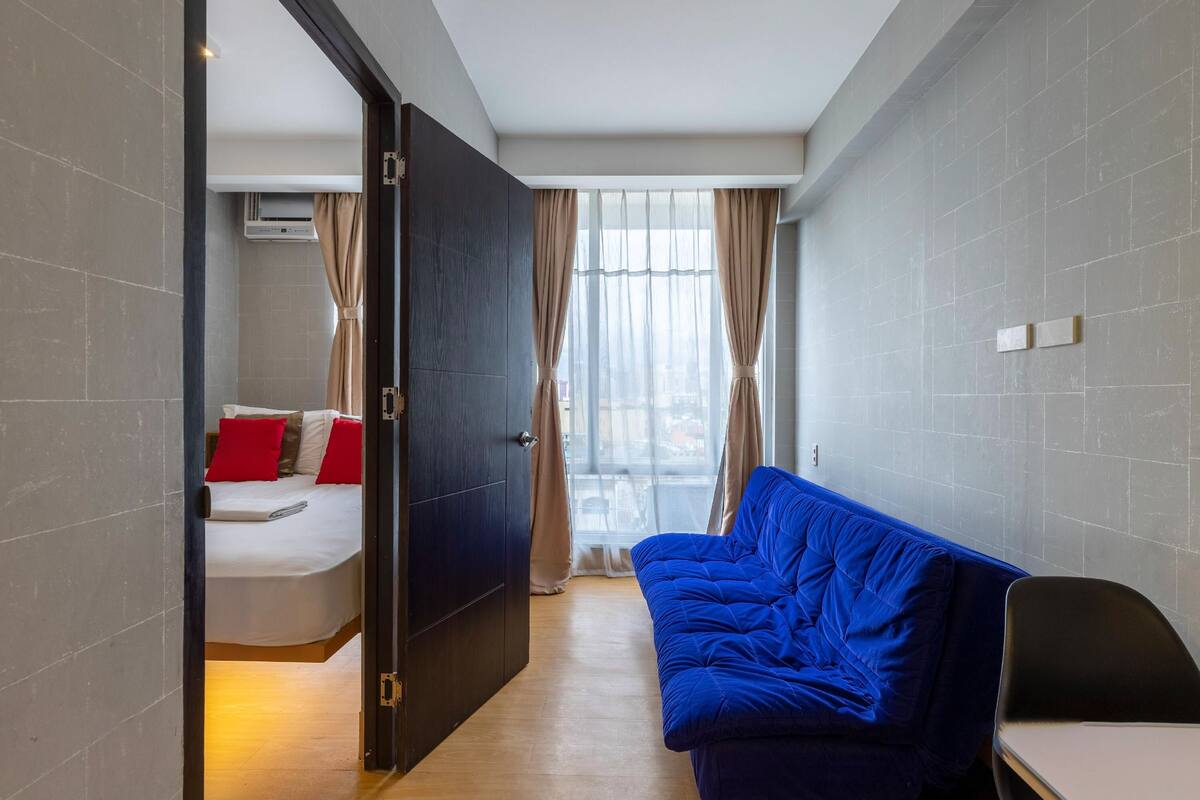 A modern hotel room with a bed, a blue sofa, and a desk.