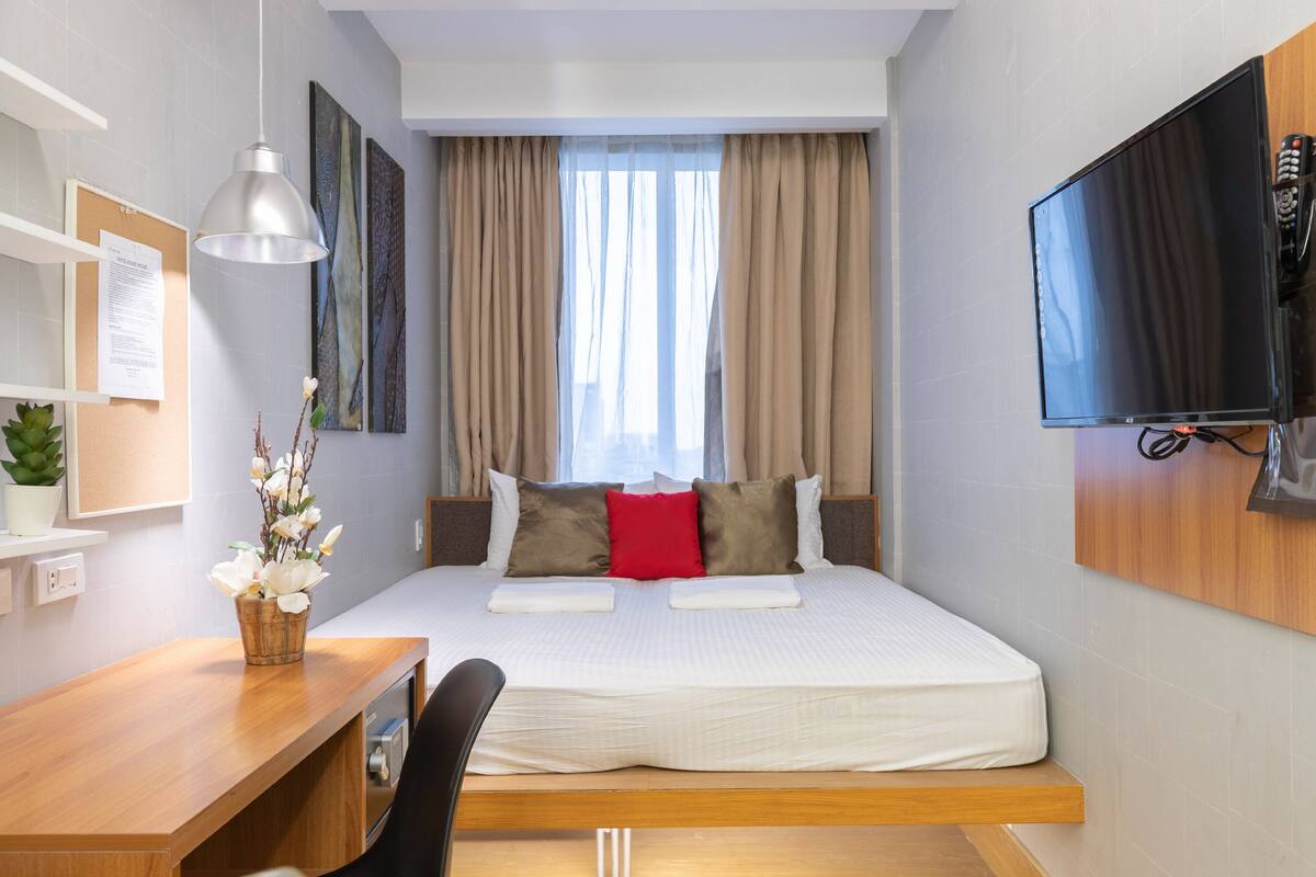 A hotel room with a bed, a desk, a chair, a TV, and a window with curtains.