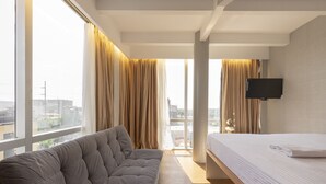 A modern bedroom with a large window, a sofa, a bed, and a TV. - Selah Pods Hotel Manila (Pasay)