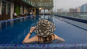 A pool area with a view of a cityscape, a covered seating area, and a person relaxing by the pool. - Selah Pods Hotel Manila (Pasay)