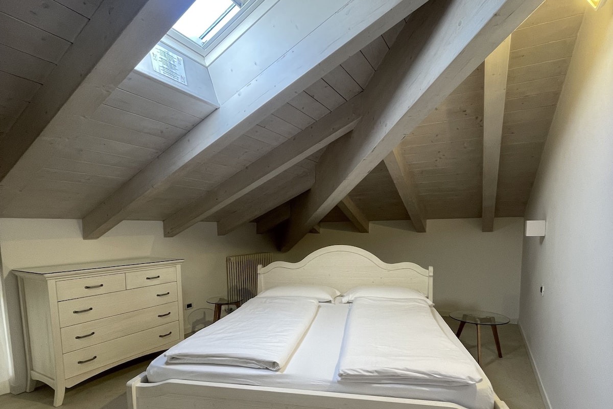 A bedroom with a sloped ceiling, a bed, a dresser, and a radiator.