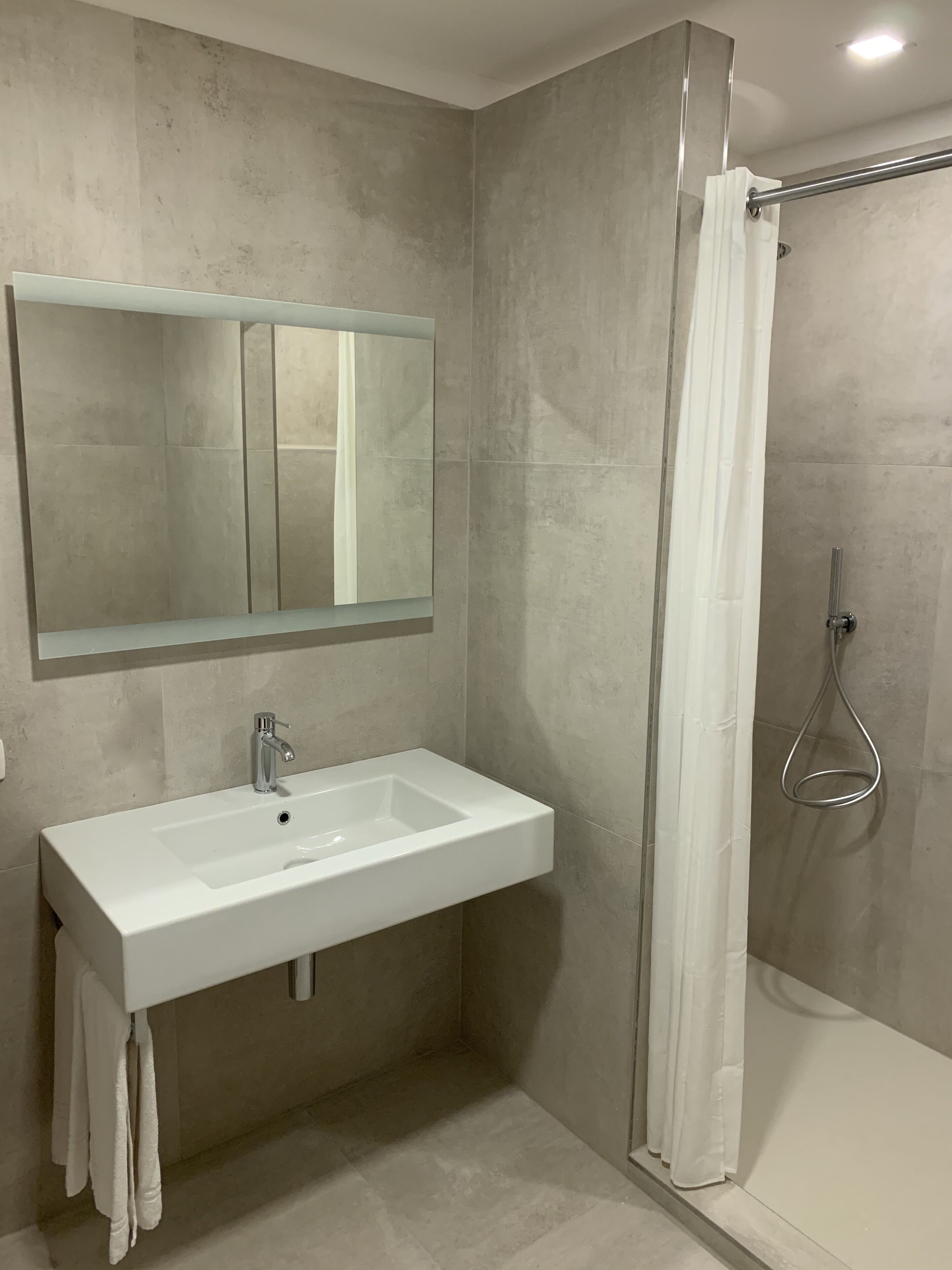 Un baño con lavamanos blanco, un espejo y zona de ducha.
