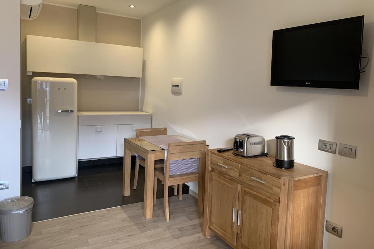 A compact kitchen with a refrigerator, a toaster, a kettle, and a wooden cabinet.