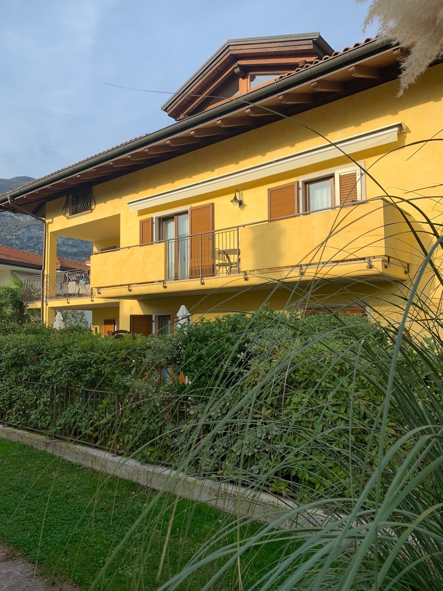 Un bâtiment jaune à deux étages, doté d’un balcon et entouré de verdure.