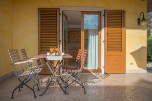 A patio with a table set for two, two chairs, and a pair of wooden shutters. - Arcovacanze (Arco)