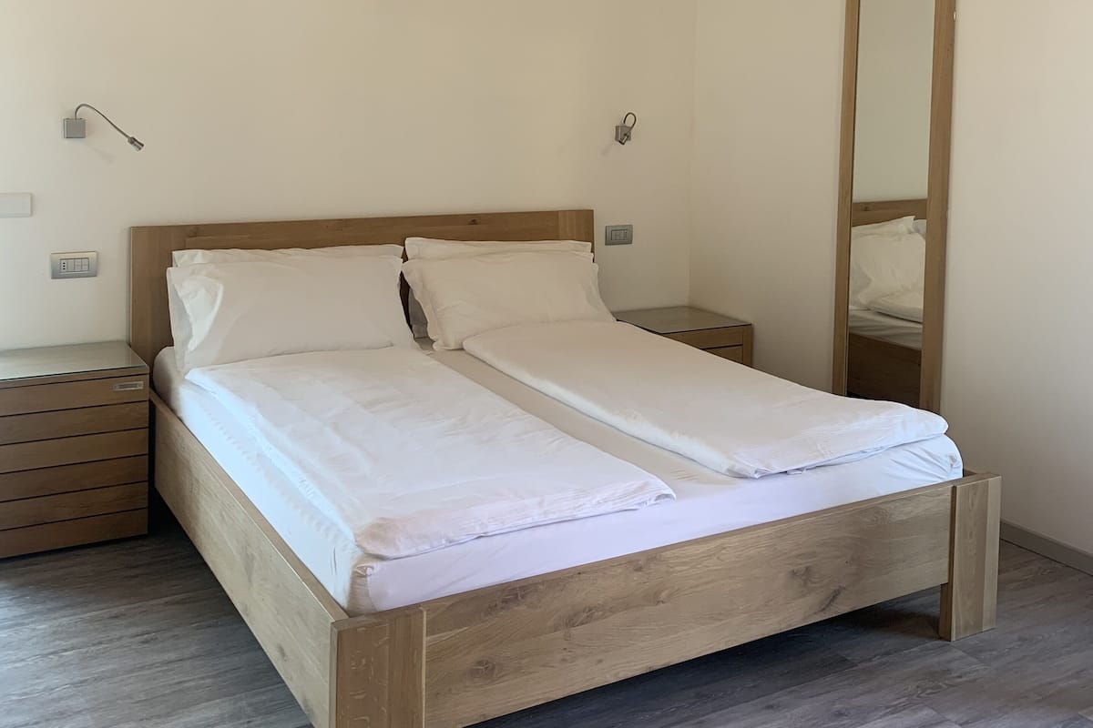 A bedroom with a wooden bed, a nightstand, a bedside table, a mirror, and a wooden ceiling.