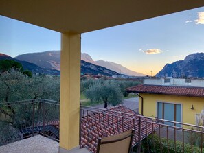A balcony with a view of mountains and a yellow building with a tiled roof. - Arcovacanze (Arco)