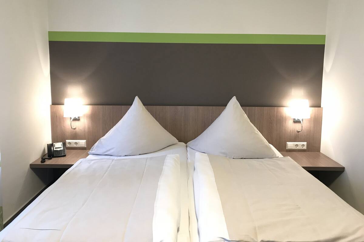 A double bed with two pillows, a wooden headboard, and two bedside lamps.
