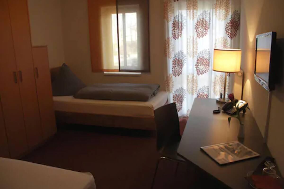 A small room with a bed, a desk, a chair, a lamp, and a TV.