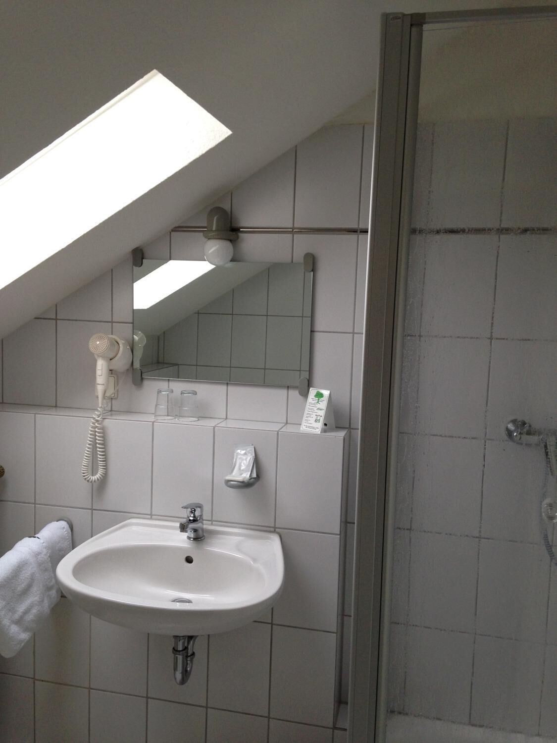 A bathroom with a skylight, a sink, a mirror, a telephone, and a shower.
