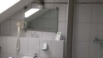 A bathroom with a skylight, a sink, a mirror, a telephone, and a shower.