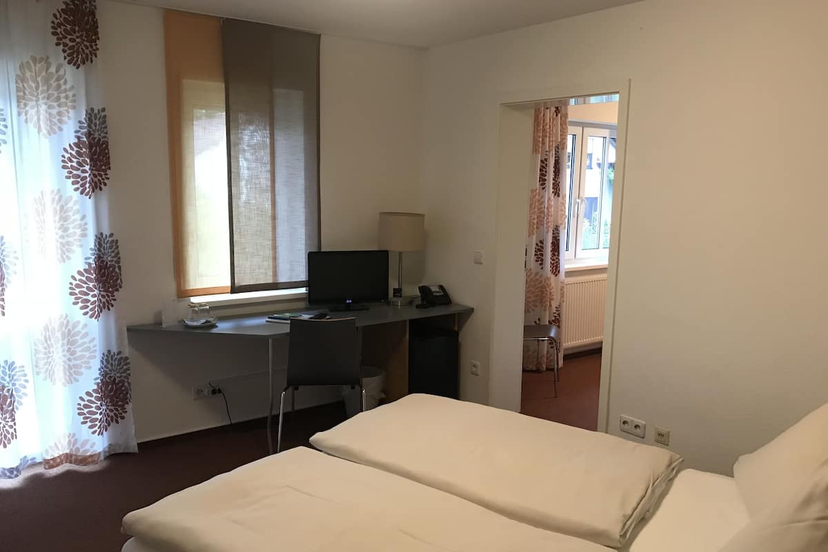 A hotel room with a bed, a desk with a computer, a lamp, and a window with curtains.