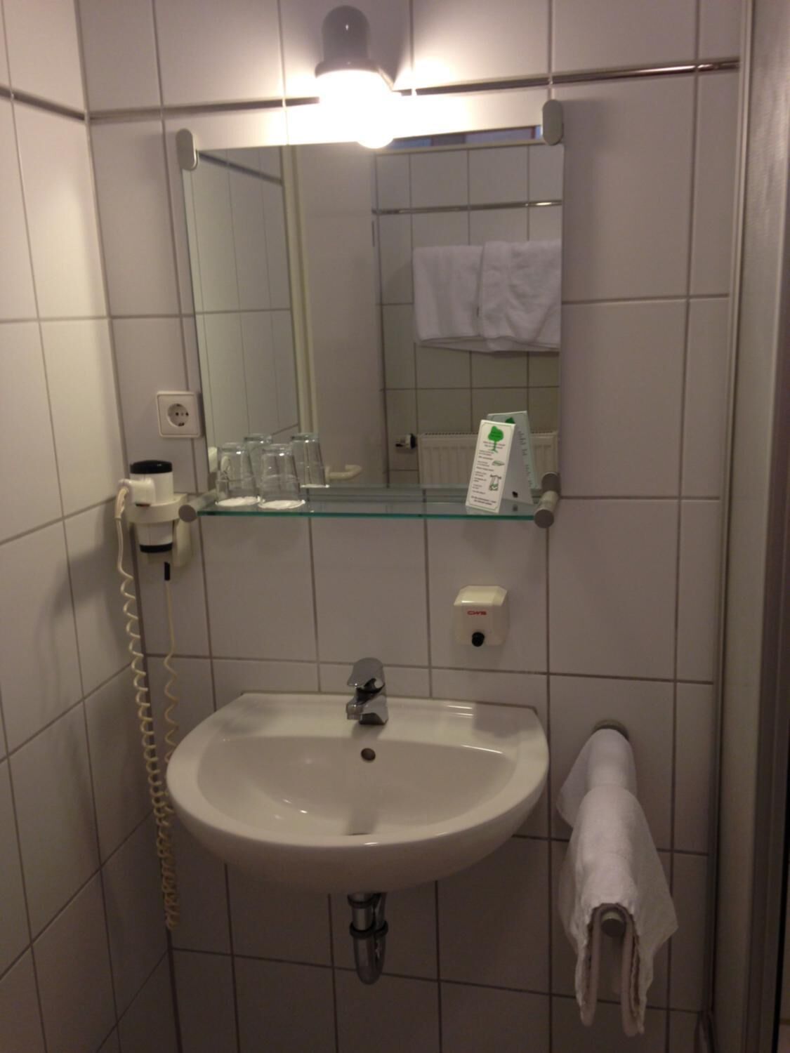 A bathroom with a white sink, a mirror, a glass shelf with toiletries, a towel rack, and a telephone.