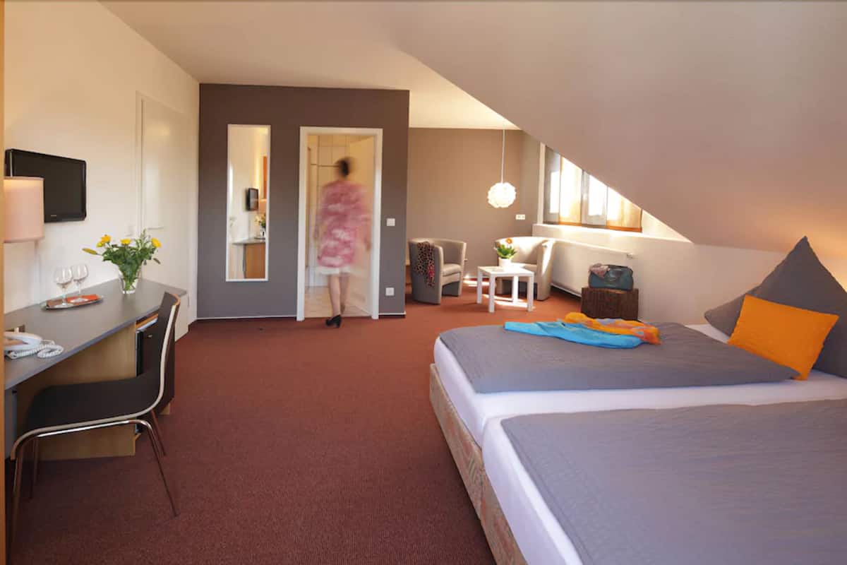 A hotel room with a bed, desk, chair, and a small seating area with a table and chairs.