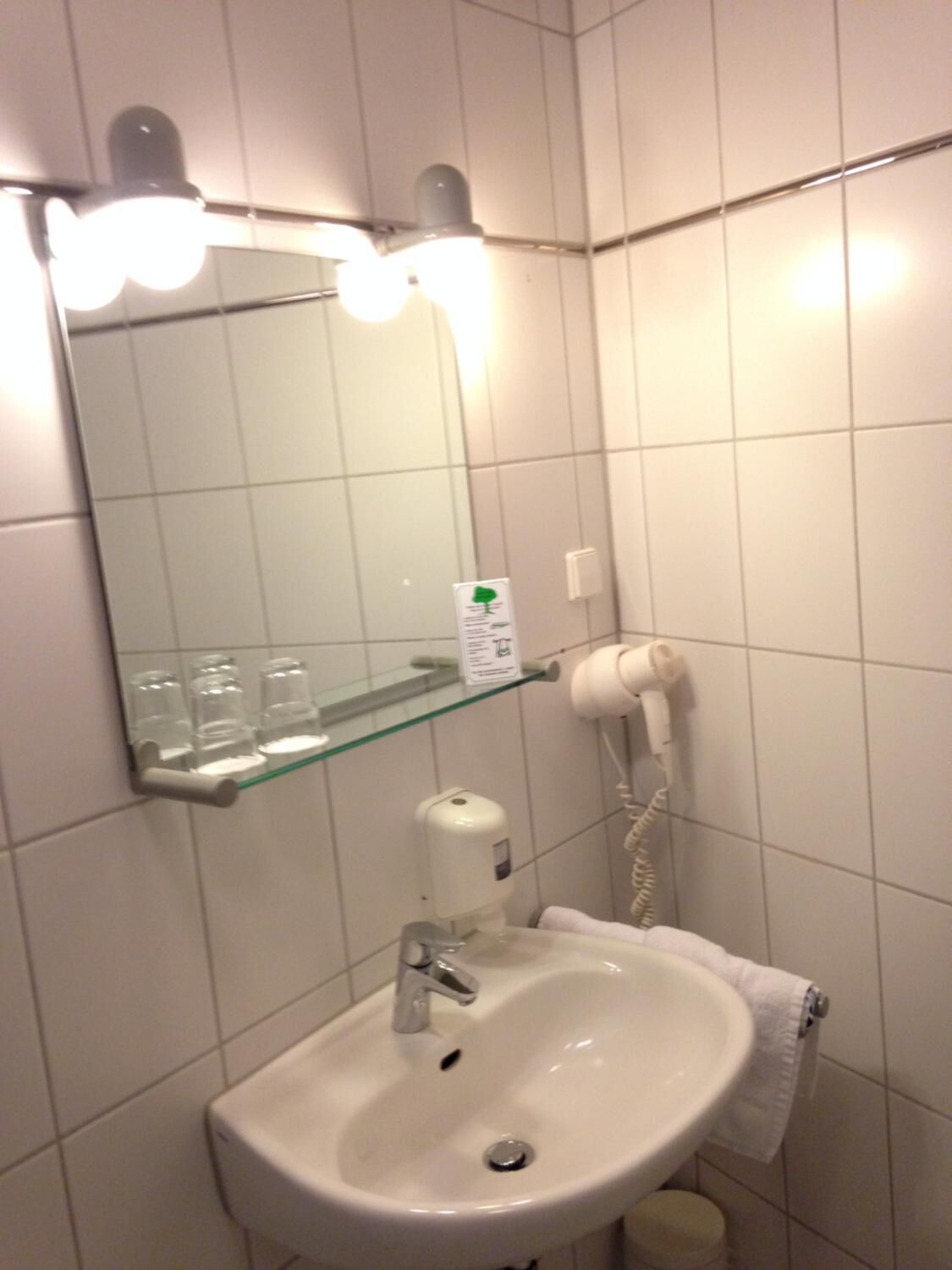 Une salle de bain avec un lavabo blanc, un miroir avec éclairage intégré, une étagère en verre, un sèche-cheveux et un téléphone.