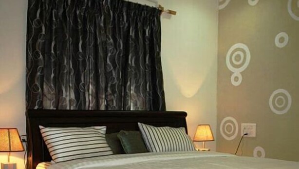 Une chambre avec un lit, deux tables de chevet, un climatiseur fixé au mur, un rideau à motifs et un mur orné de motifs circulaires.