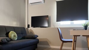 Una sala moderna con un sofá azul oscuro, una mesa de comedor de madera y un televisor montado en la pared.