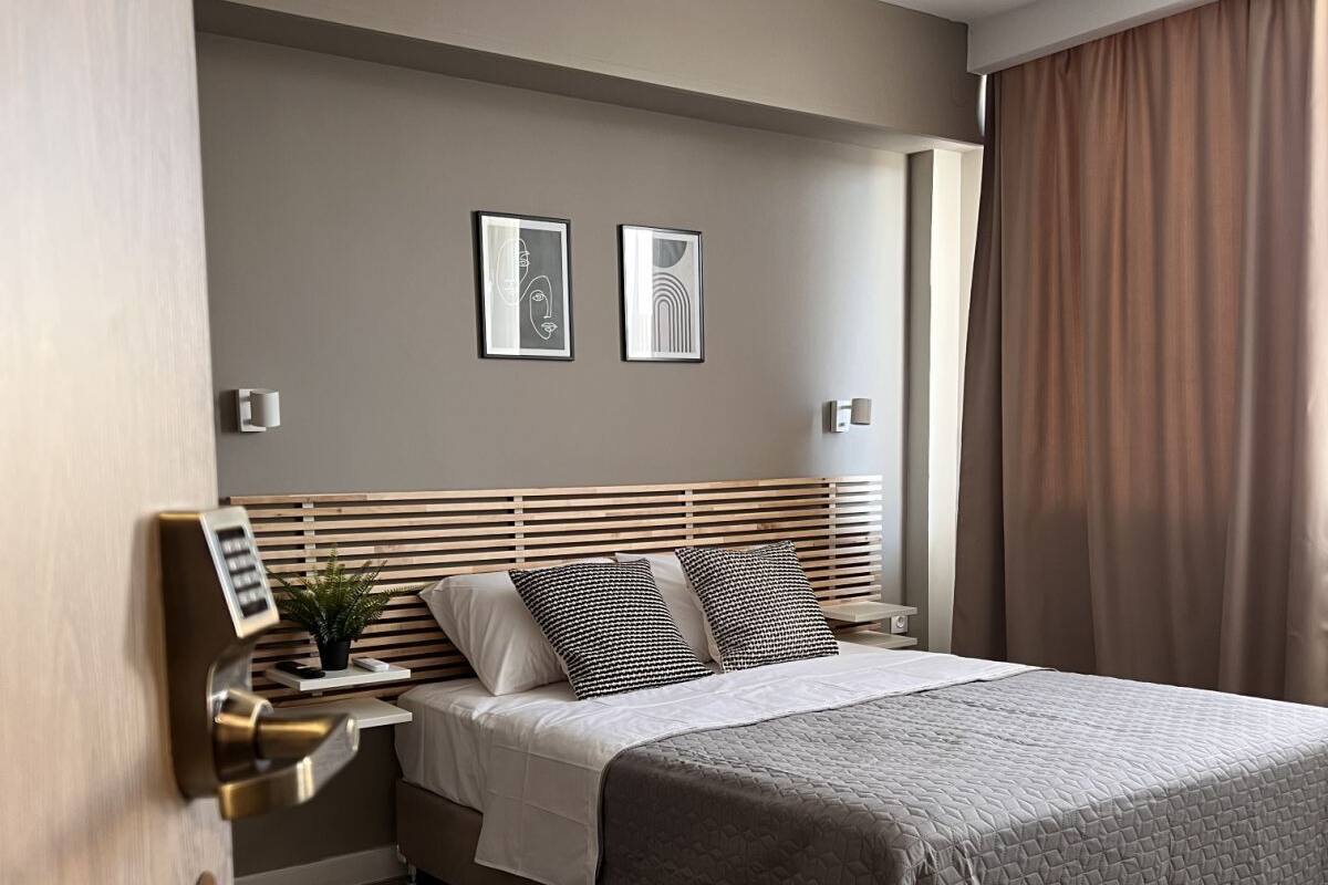 Una habitación de hotel moderna con cabecera de madera, una cama grande, una mesita de noche con lámpara y dos cuadros enmarcados en la pared.