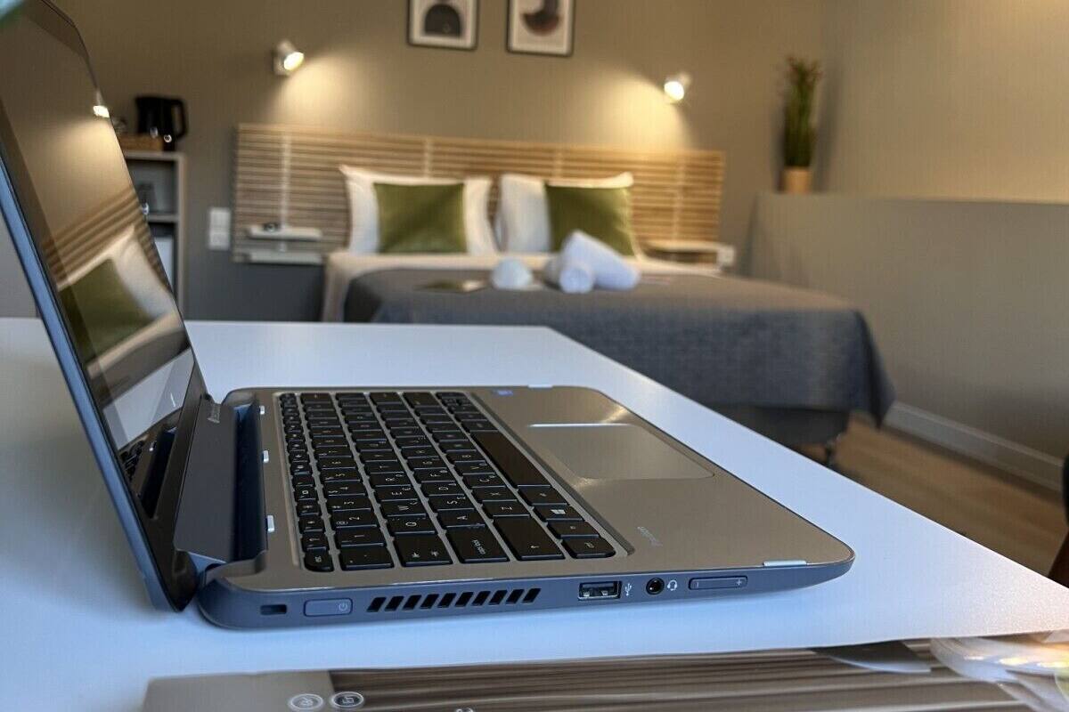 Una laptop sobre un escritorio con una cama al fondo.