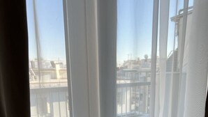 Vista a través de una ventana que muestra un paisaje urbano, con edificios y un balcón.